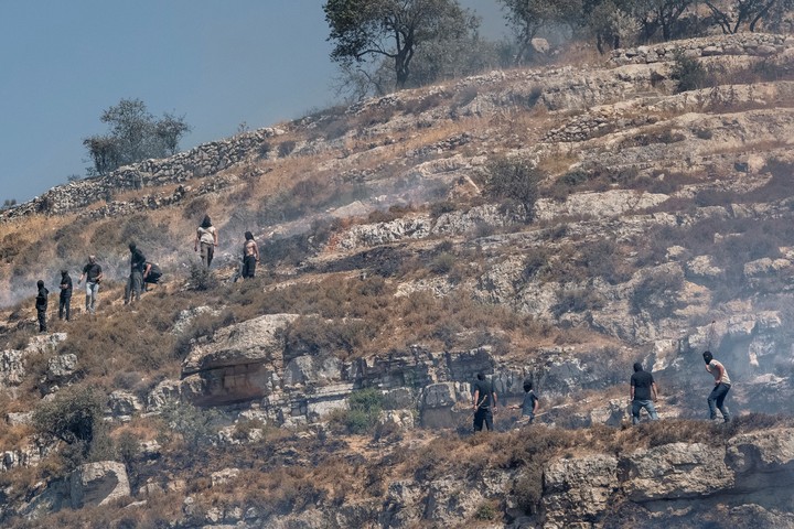 Colonos enmascarados lanzan piedras contra palestinos en Sinjil, Cisjordania, el 3 de julio de 2025. (Daniel Berehulak/The New York Times)
