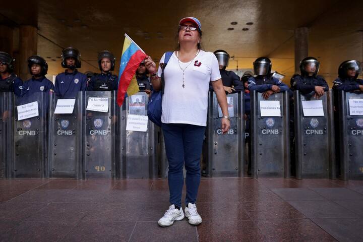 Una mujer sostiene una bandera venezolana frente a una fila de la Policía Nacional Bolivariana de Antidisturbios durante una protesta para exigir la renuncia del presidente del Consejo Nacional Electoral (CNE), Elvis Amoroso, la liberación de los presos políticos y nuevas elecciones presidenciales, frente a la sede del CNE en Caracas, Venezuela, el 1 de octubre de 2026. REUTERS/Gaby Oraa